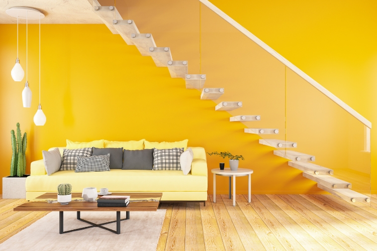 Modern nappali élénk napsárga falfestéssel, amely magas fényvisszaverő képességével világosabb hatást kelt; a homogén, sima felület kiemeli a lépcsőszerkezet letisztult vonalait.